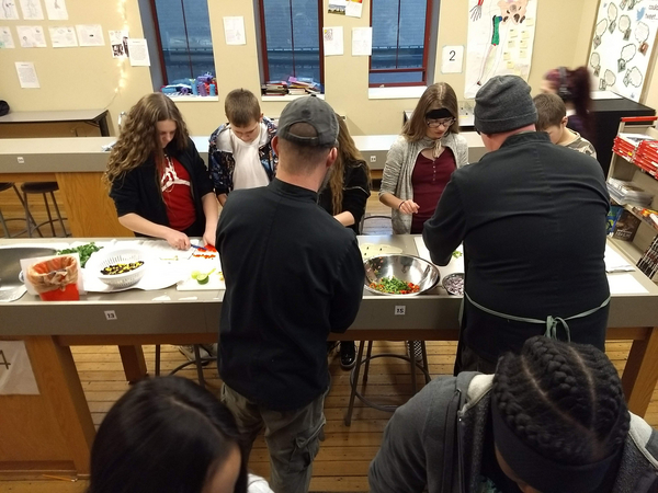 Four high school students chopping something red while two chefs assist