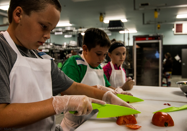 Three kids use green, safety knives to cut vegetables